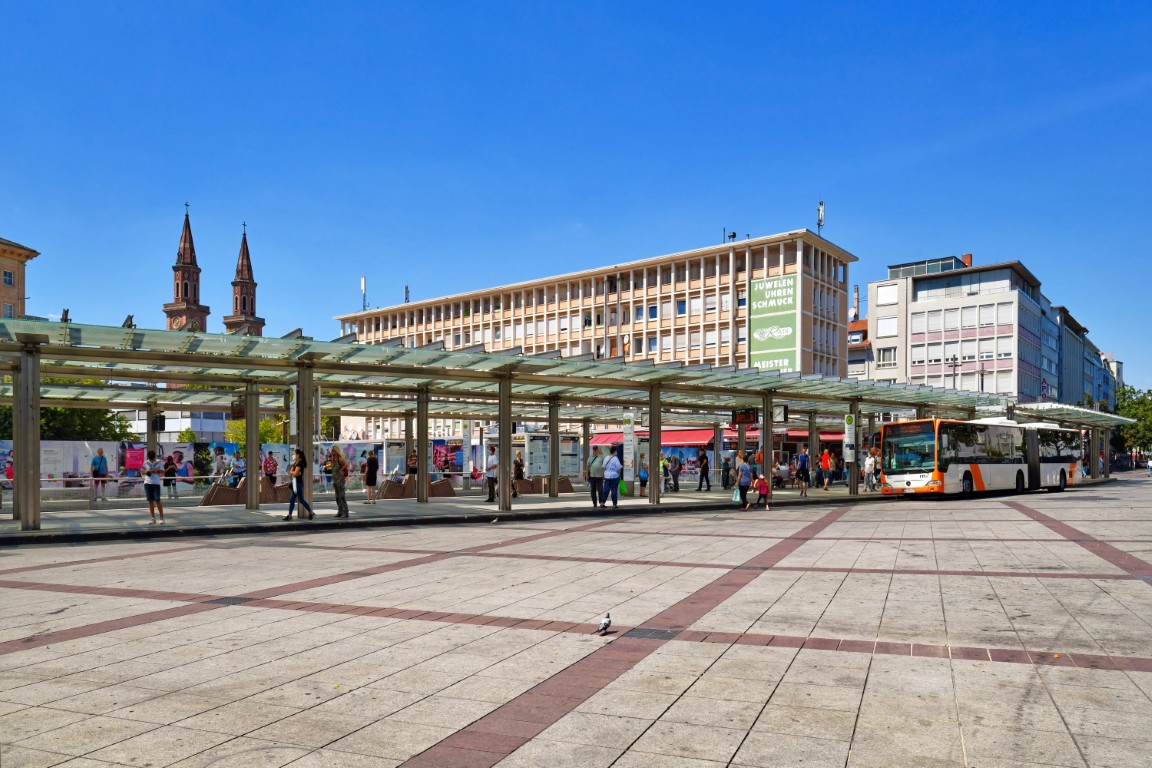 Platz mit Bus, Personen, moderner Architektur und Kirchtürmen
